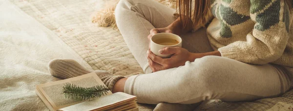 Acogedora casa. Hermosa chica está leyendo un libro en la cama. Buenos días con el té. Una chica joven y bonita relajándose. El concepto de lectura — Foto de Stock