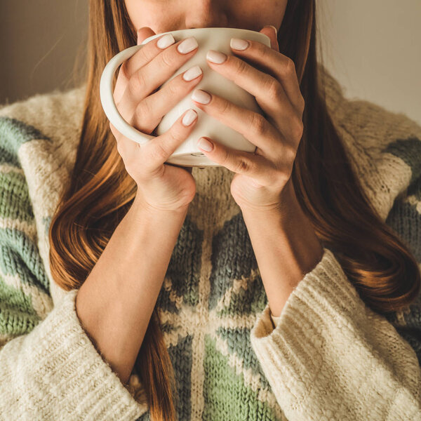 Cozy home. Woman with cup of hot drink  by the window. Looking at window and drink tea. Good morning with tea. Young girl relaxing