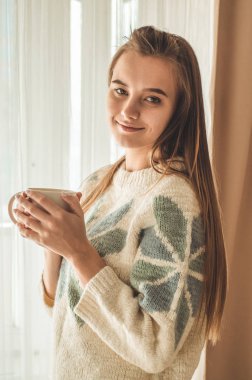 Rahat ev. Pencere kenarındaki sıcak içecek bir kadınla. Pencere ve içecek çay arıyorum. Günaydın çay ile. Genç kız rahatlatıcı