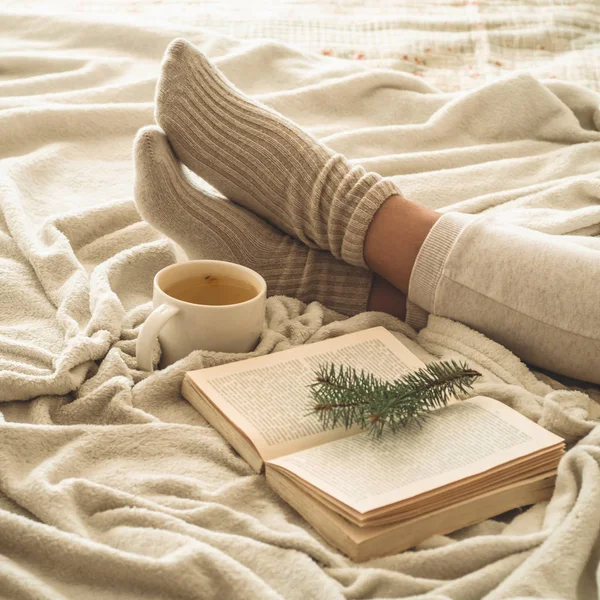 Cozy winter evening , warm woolen socks. Woman is lying feet up on white shaggy blanket and reading book. Cozy leisure scene — Stock Photo, Image