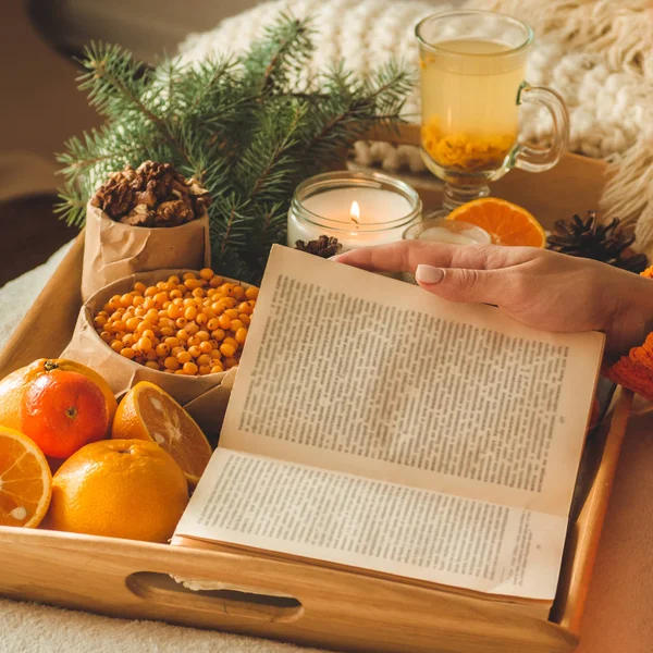 Weiche gemütliche Foto von Frau in warmem orangefarbenen Pullover auf dem Bett mit einer Tasse Tee und Obst. Mädchen sitzt auf dem Bett mit alten Büchern. — Stockfoto