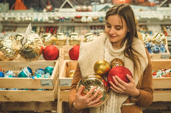 Chica con un abrigo caliente sosteniendo una bola grande para el árbol de Navidad en un centro comercial en la Feria de Navidad — Foto de Stock