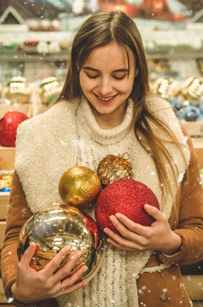 Chica con un abrigo caliente sosteniendo una bola grande para el árbol de Navidad en un centro comercial en la Feria de Navidad — Foto de Stock