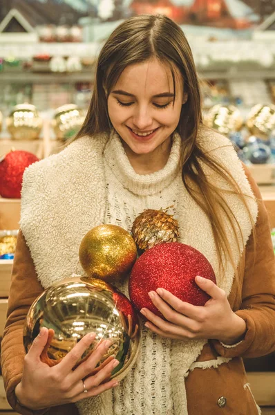 Chica con un abrigo caliente sosteniendo una bola grande para el árbol de Navidad en un centro comercial en la Feria de Navidad — Foto de Stock