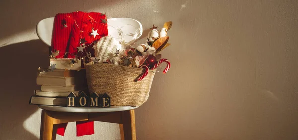 Téli pulóver meghatározott egy széken, egy kosár karácsonyi díszek, könyvek. A felirat haza nyaralás dekoráció. — Stock Fotó
