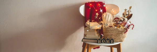 Pull d'hiver posé sur une chaise avec un panier de décorations de Noël, livres. Décoration de vacances avec l'inscription HOME . — Photo