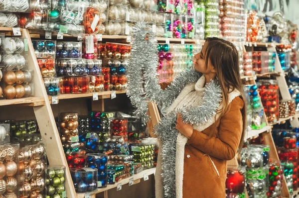 Wanita memilih Tinsel untuk pohon Natal di toko. Dekorasi tahun baru. Perak, karangan bunga berwarna. Tinsel Christmas Garland — Stok Foto