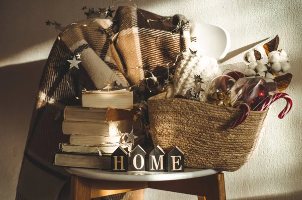 Selimut hangat musim dingin di kursi dengan sekeranjang dekorasi Natal, buku dan lampu senar. Rumah. Bacaan musim dingin. Rumah — Stok Foto