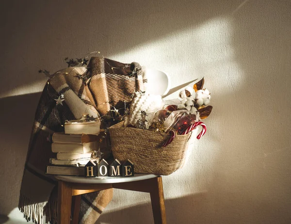 Couverture chaude d'hiver sur une chaise avec un panier de décorations de Noël, des livres et des lumières à cordes led. À la maison. Lecture d'hiver. Maison — Photo