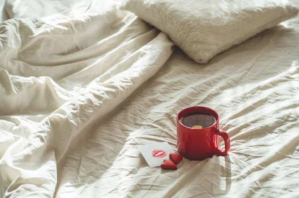 Röd kopp te och två hjärtan cookies, en anteckning med en kyss på en vit säng. Alla hjärtans dag koncept — Stockfoto