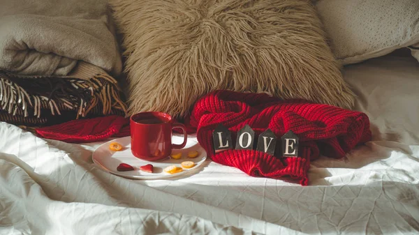 Красная чашка чая с квасом на тарелке и два сердечка со словом LOVE на белой кровати. День святого Валентина . — стоковое фото