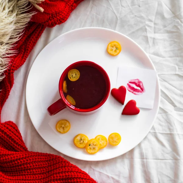 Красная чашка чая с кумкватом и печеньем с двумя сердцами, записка с поцелуем на белой кровати. День святого Валентина — стоковое фото
