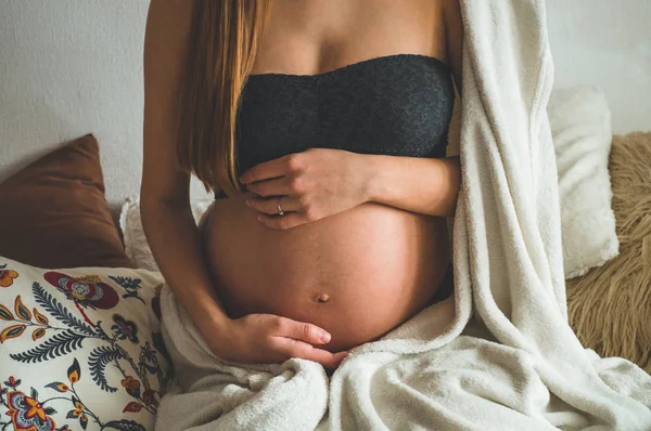 Jolie femme enceinte est assise dans son lit et tenant son ventre. Derniers mois de grossesse. — Photo