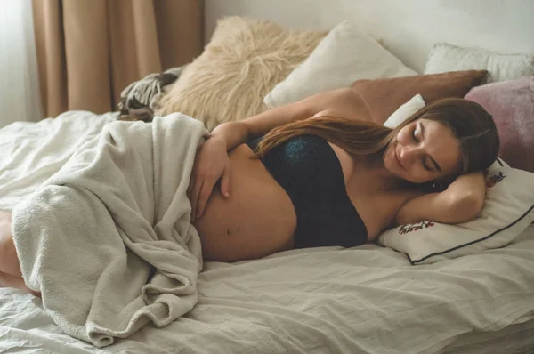 Mulher grávida atraente está deitada na cama e segurando sua barriga. Últimos meses de gravidez . — Fotografia de Stock