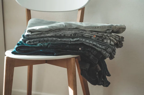 Jeans denim cloth garment monochrome gray blue linen textile stacked on wooden chair near white wall pile concept — Stock Photo, Image