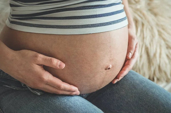 Atractiva mujer embarazada está sentada en la cama y sosteniendo su vientre — Foto de Stock