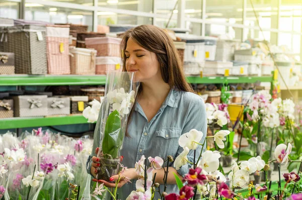 Hermosa cliente femenino oliendo orquídeas florecientes coloridas en la tienda al por menor . — Foto de Stock