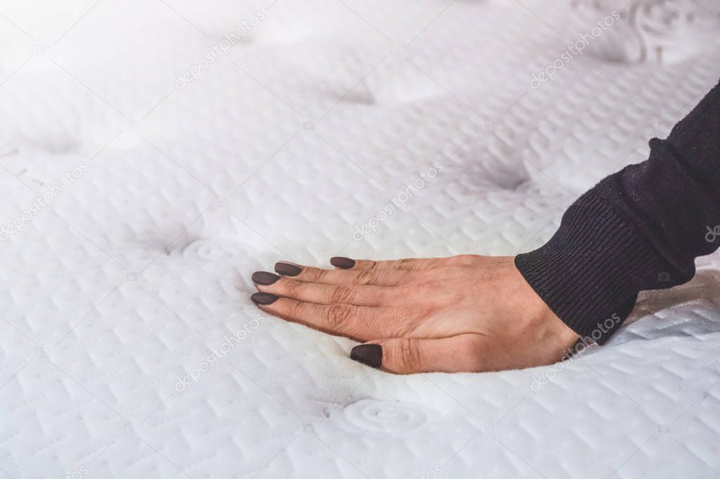 Beautiful girl touches the mattress. She examines the mattress she wants to buy