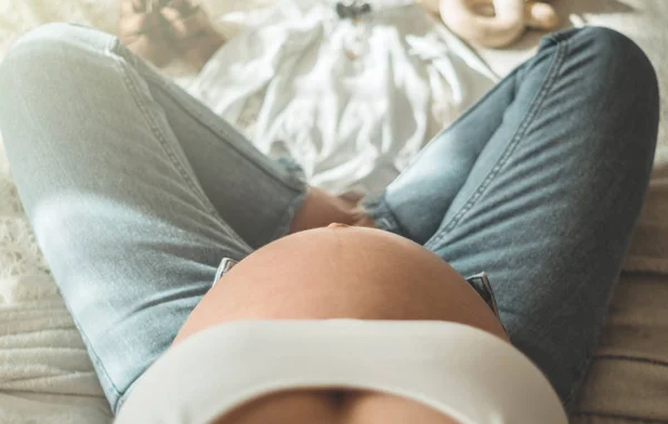 Belle femme enceinte assise sur un lit et regarde un enfant. Attentes. Concept de grossesse — Photo