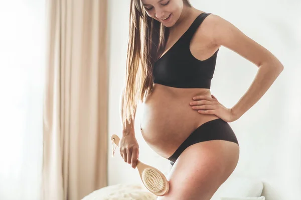 Schwangerschaft und Trockenmassage. Schwangerschaft Frau hält trockene Bürste oben auf ihr Bein — Stockfoto