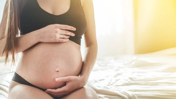 Attrayant femme enceinte est assis dans le lit et tenant son ventre . — Photo