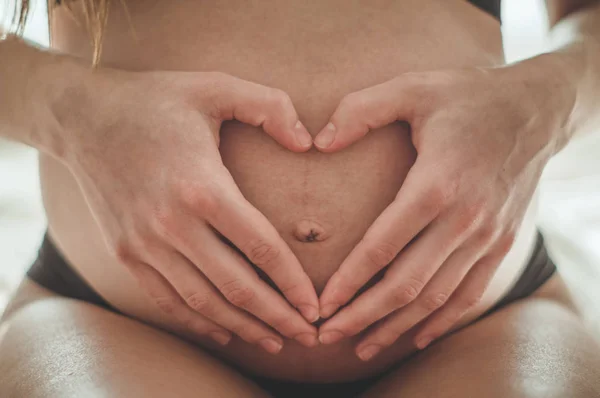 Mulher grávida atraente está sentado na cama e segurando sua barriga . — Fotografia de Stock