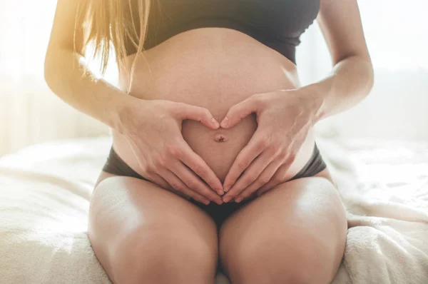 Atractiva mujer embarazada está sentada en la cama y sosteniendo su vientre . — Foto de Stock