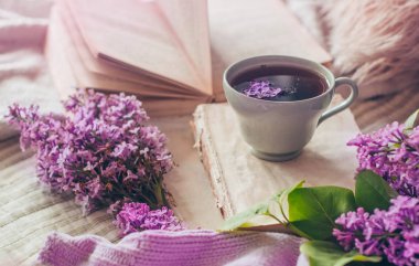 Oturma odasının ev iç natürmort detayları. Kitaplarda leylak çiçekleri ve bahar dekoru ile kazak ve çay fincan