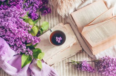 Oturma odasının ev iç natürmort detayları. Kitaplarda leylak çiçekleri ve bahar dekoru ile kazak ve çay fincan