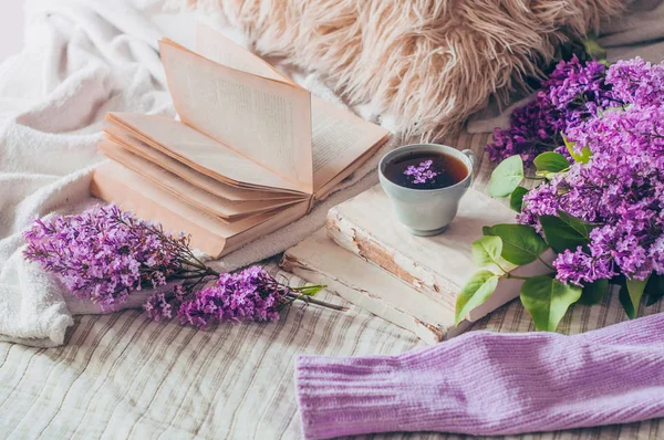 Stillleben Details im Wohnbereich des Wohnzimmers. Pullover und Tasse Tee mit fliederfarbenen Blumen und Frühlingsdekor auf den Büchern — Stockfoto