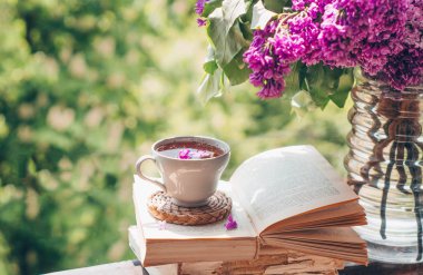 Kitap, bardak, bir fincan çay ve tahta bir pencerede leylak. Bahçede güzel kokulu çay. Romantik kavram