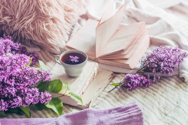 Stillleben Details im Wohnbereich des Wohnzimmers. Pullover und Tasse Tee mit fliederfarbenen Blumen und Frühlingsdekor auf den Büchern — Stockfoto