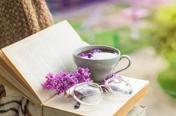 Buch, Gläser, eine Tasse Tee und Flieder auf einem Holzfenster. Duftender Tee im Garten. Romantisches Konzept — Stockfoto