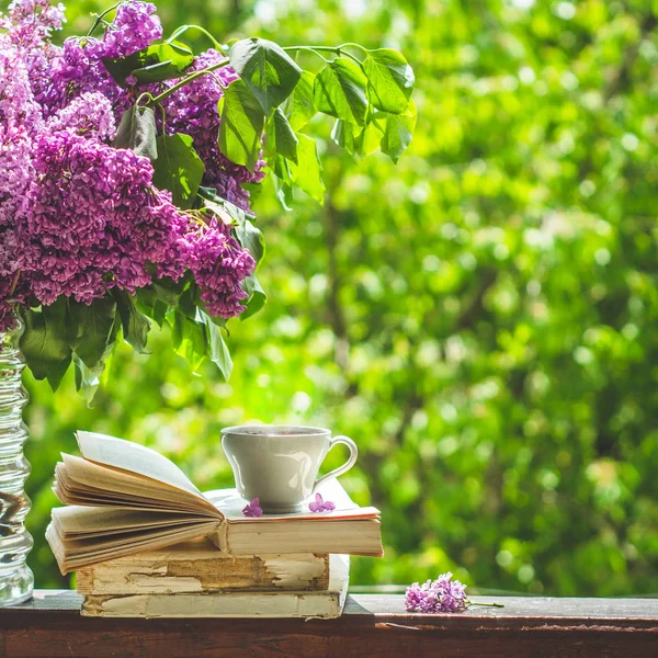 Buch, Gläser, eine Tasse Tee und Flieder auf einem Holzfenster. Duftender Tee im Garten. Romantisches Konzept — Stockfoto