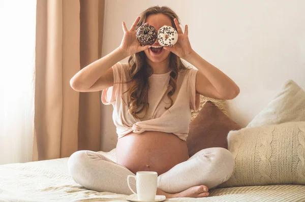 Pregnancy and nutrition. Pregnant woman enjoying donuts and tea in bed, free space. Concept of expectation and health — Stock Photo, Image