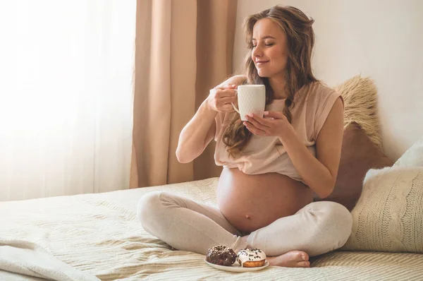 Embarazo y nutrición. Mujer embarazada disfrutando de donas y té en la cama, espacio libre. Concepto de expectativa y salud — Foto de Stock