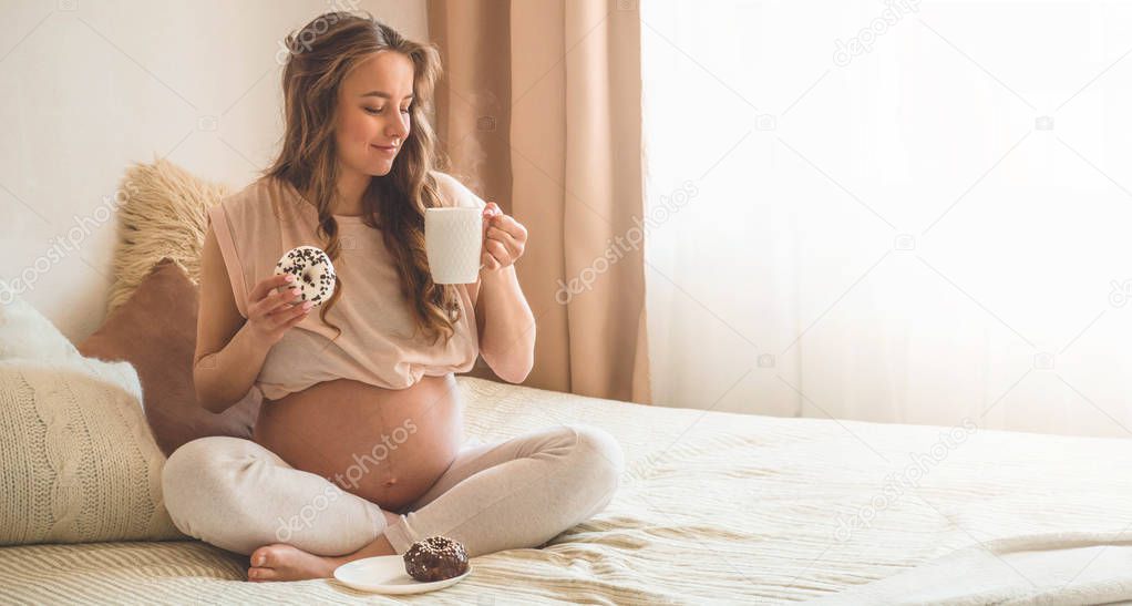 Pregnancy and nutrition. Pregnant woman enjoying donuts and tea in bed, free space. Concept of expectation and health