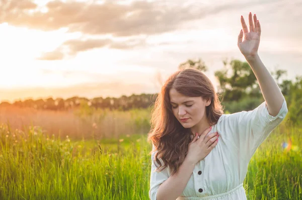 Gadis menutup matanya, berdoa di lapangan selama matahari terbenam yang indah. Tangan dilipat dalam konsep doa untuk iman — Stok Foto