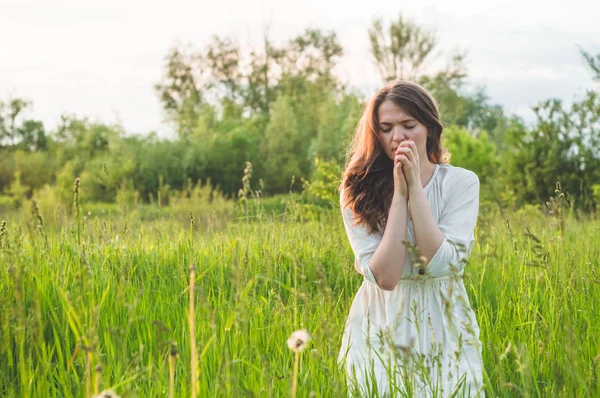 Girl closed her eyes, praying in a field during beautiful sunset. Hands folded in prayer concept for faith Royalty Free Stock Images