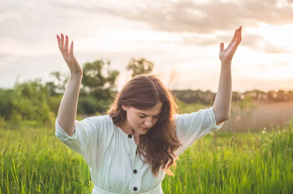 La jeune fille ferma les yeux, priant dans un champ pendant un beau coucher de soleil. Les mains jointes dans le concept de prière pour la foi Images De Stock Libres De Droits