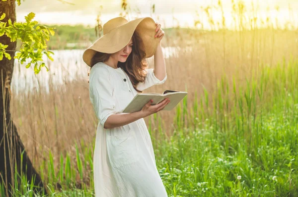 Hermosa chica en el campo leyendo un libro. La chica sentada en una hierba, leyendo un libro. Descanso y lectura — Foto de Stock