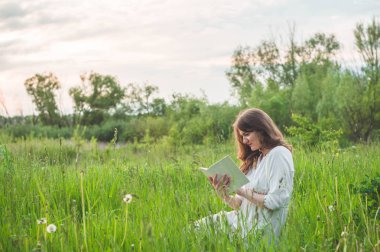Sahada kitap okuyan güzel bir kız. Çimlerin üzerinde oturan, kitap okuyan kız. Dinlenme ve okuma