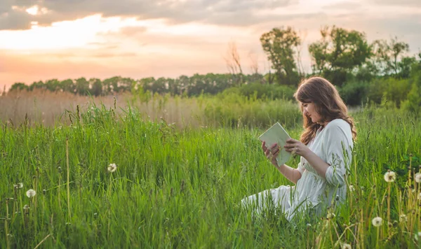 Mooi meisje in het veld het lezen van een boek. Het meisje zittend op een gras, het lezen van een boek. Rusten en lezen — Stockfoto