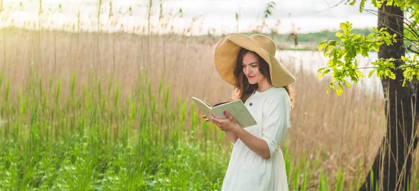 Menina bonita no campo lendo um livro. A rapariga sentada numa relva, a ler um livro. Descanso e leitura — Fotografia de Stock