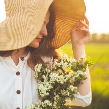 Vintage elbise ve alan kır çiçekleri hasır şapka güzel genç gülümseyen kadın. Kız elinde çiçeklerle dolu bir sepet tutuyor.