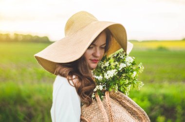 Vintage elbise ve alan kır çiçekleri hasır şapka güzel genç gülümseyen kadın. Kız elinde çiçeklerle dolu bir sepet tutuyor.