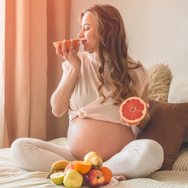 Pregnancy and healthy organic nutrition. Pregnancy and grapefruit. Pregnant woman enjoying fresh fruits in bed, free space.