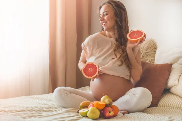 Εγκυμοσύνη και υγιής βιολογική διατροφή. Εγκυμοσύνη και γκρέιπφρουτ. Έγκυος γυναίκα που απολαμβάνει φρέσκα φρούτα στο κρεβάτι, ελεύθερος χώρος. — Φωτογραφία Αρχείου