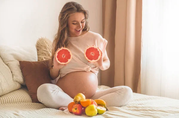 Embarazo y nutrición orgánica saludable. Embarazo y pomelo. Mujer embarazada disfrutando de frutas frescas en la cama, espacio libre . — Foto de Stock