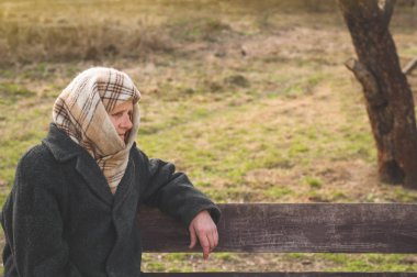 Ciddi yaşlı bir kadın bankta oturup başka bir yere bakıyor. Bastona yaslanmış düşünceli yaşlı büyükanne portresi